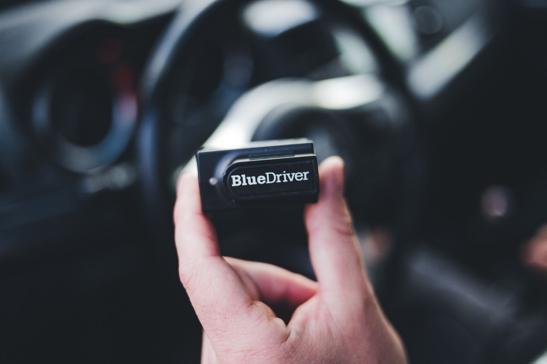 Dłoń trzyma skaner Bluedriver OBD2 wewnątrz wnętrza samochodu