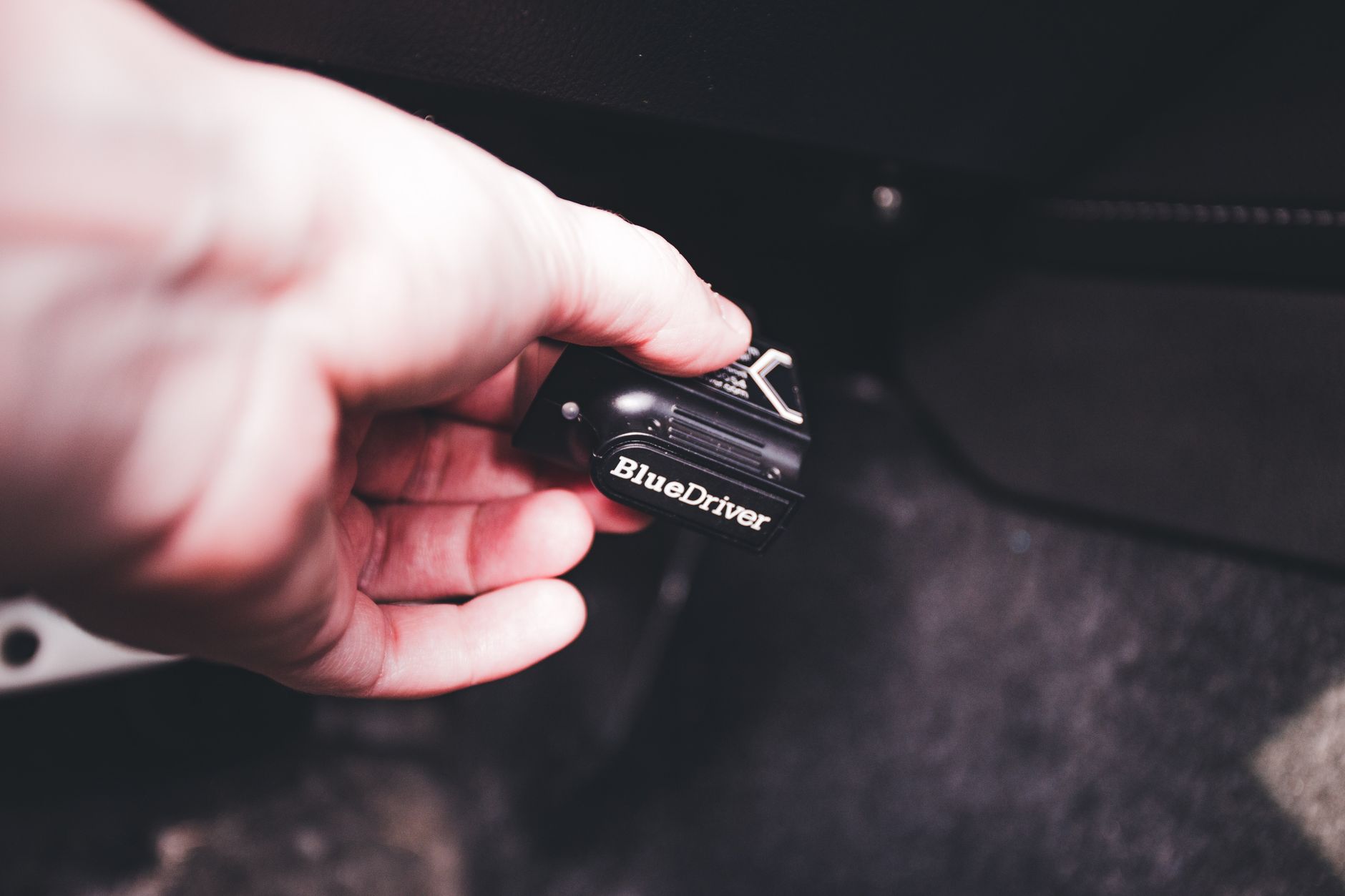 Ręka podłączająca adapter diagnostyczny BlueDriver do gniazda OBD w aucie